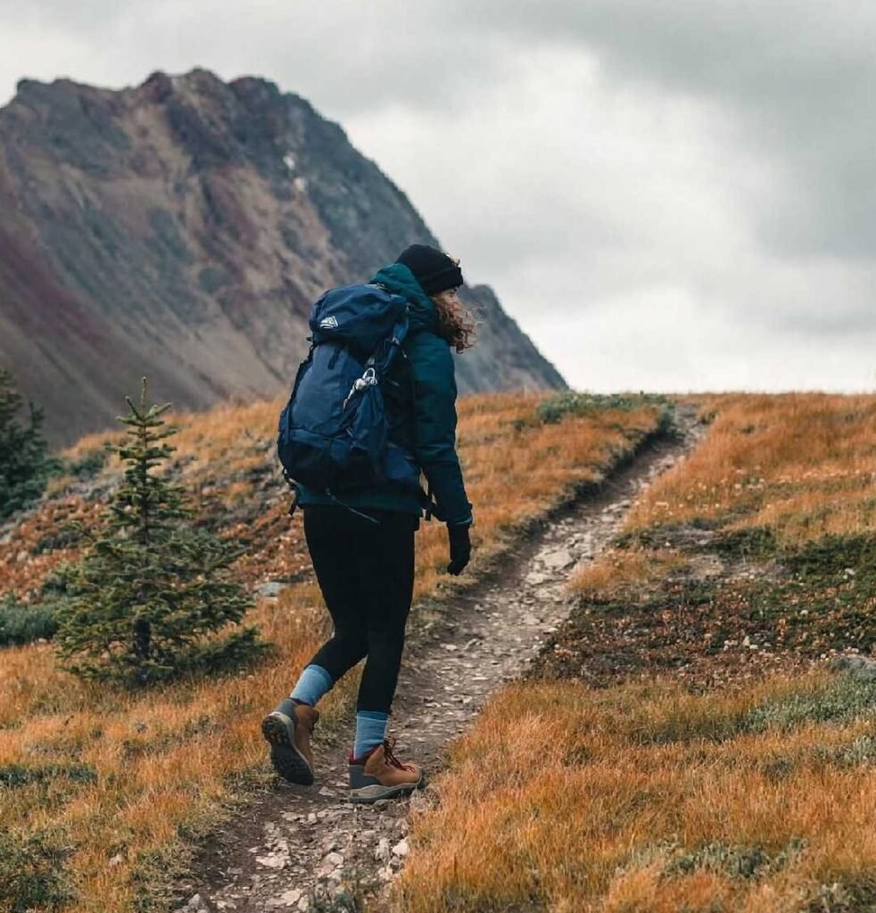 Woman hiking on a mountain trail with a backpack and rugged mountain scenery in the background.